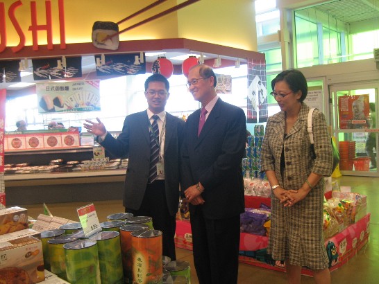 大統華超市渥太華分店店長文繼明向李代表及夫人介紹美食展攤位與內容。