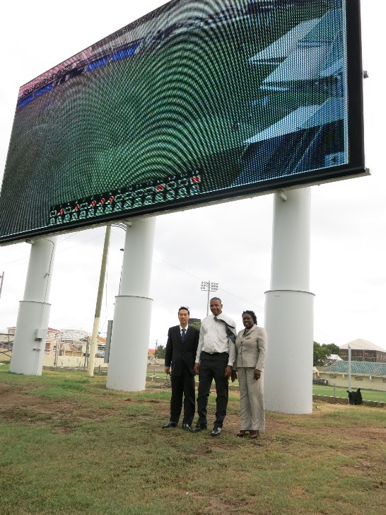 保全監視系統監視畫面投射於Warner Park體育場戶外大型螢幕。曹大使與克國國安次長Astona Browne(右1)大使及科技體育部長Glenn Phillip(中)於螢幕前合影。