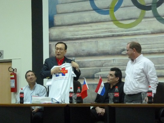 劉大使與記者會中說明T恤設計涵義。右一為巴奧委會主席Camilo Pérez，右二為體育部長Víctor Pecci。