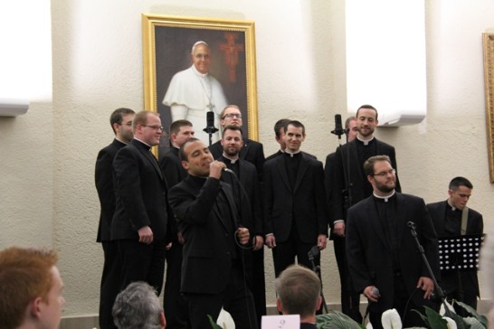 A solo singer accompanied by a chorus of seminarians entertains the public.