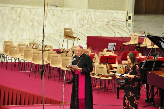 教廷醫療牧靈委員會主席Zygmunt ZIMOWSKI總主教（左）以麥克風向全場數千名觀眾介紹來自中華民國之雙鋼琴家葉綠娜女士及其德籍夫婿魏樂富（Rolf-Peter Wille）先生將上台演奏。右為義國知名藝人Claudia Koll女士。