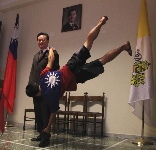 廖宏淋在大使館內表演「國旗飄」特技，他係以王大使（左）為支撐點，撐住全身和地面平行，看來就像一面人型國旗，因此友人都戲稱他是「阿飄男」