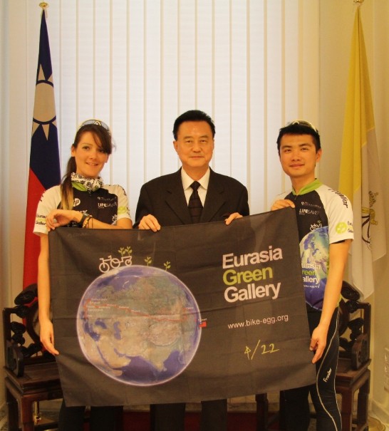 王豫元大使（中）與「綠色騎跡」單車隊隊員張晏鐘先生（右）及花樂梅女士（左）在大使館內共持車隊旗幟合影