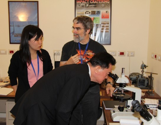王豫元大使（中）在Consolmagno先生（右後）向王品方小姐（左後）解說隕石來歷時用顯微鏡觀察有45億年歷史的黝黑隕石