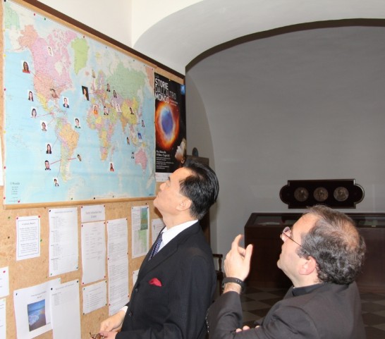天文台台長Funes神父（右）在公佈欄以研習營25位學生照片標出國籍之世界地圖向王豫元大使（左）介紹來自各大洲23國的學生