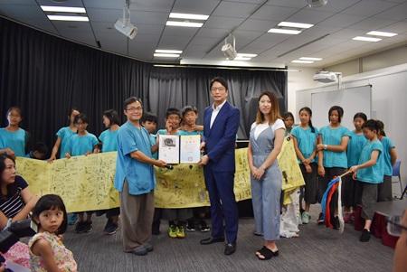 張仁久・駐日副代表（写真前列中央）、宜蘭県岳明小学校の李公元先生（前列左）、日本から宜蘭県蘇澳鎮の浜辺に漂着したカメラを拾ったことが縁で来日し、環境保護の大切さを呼びかけた人形劇を披露した同校６年の児童たち、カメラの落とし主 椿原世梨奈さん（前列右）
