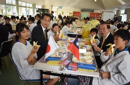 茨城県笠間市立稲田小学校で開催された交流給食会で、行政院農業委員会農糧署から提供された台湾バナナを同校の児童らと味わう謝長廷・駐日代表（写真右２）、山口伸樹・笠間市長（左２）
