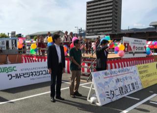 李世丙・駐大阪弁事処長(左1)と尾崎正直・高知県知事(右1)が高知駅前の広場で新竹県尖石鄉玉峰小学校タイヤル族舞踊団のパフォーマンスに声援を送る様子