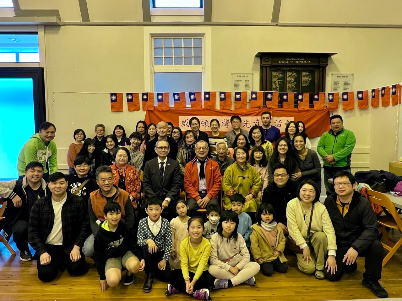 駐紐西蘭陳克明代表（次排著西裝）與威靈頓台灣華光協會李會長仁皓（前排蹲著並著橘背心）暨該會鄉親、本處同仁合影