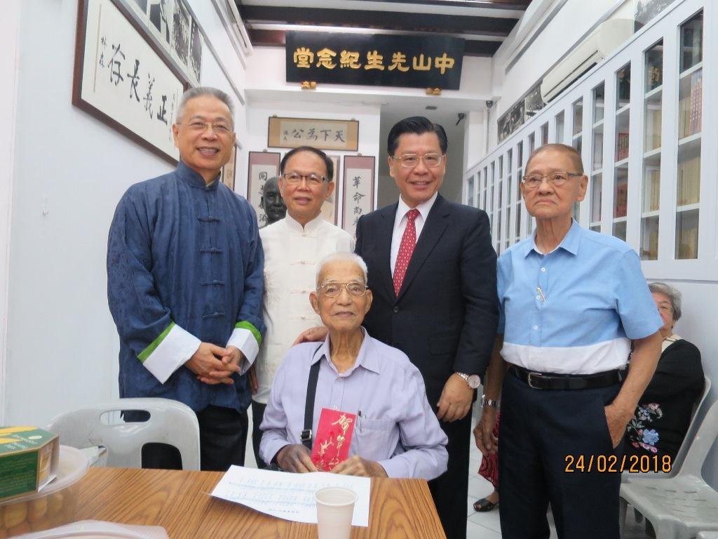 本處梁代表國新(站立者右2)致贈新年紅包予新加坡同德書報社高齡99歲的名譽社長吳少強(前排坐者)。