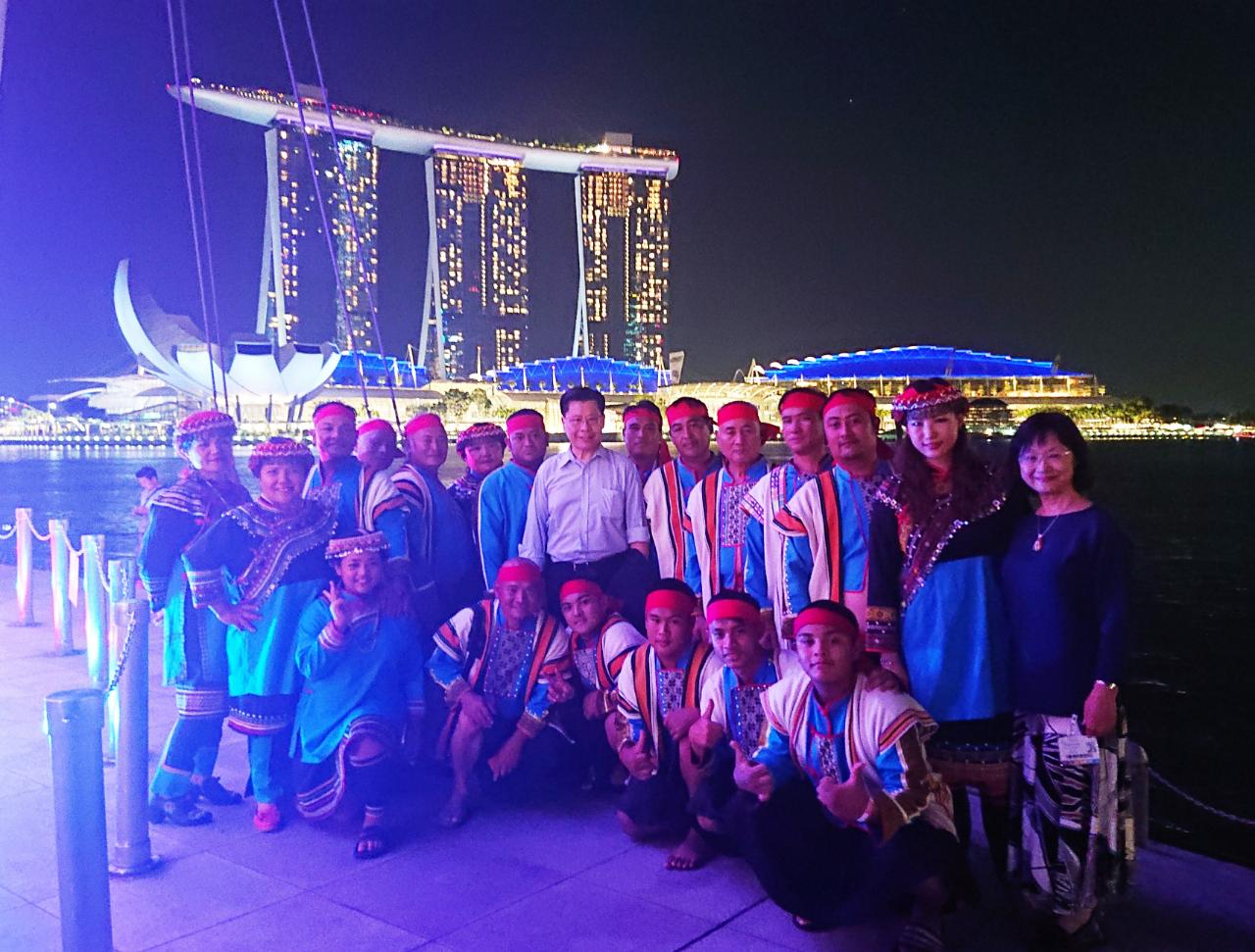 駐新加坡台北代表處代表梁國新(第二排中)於108年4月21日與臺東布農族八部合音、大提琴家張道文(第二排右二)、製作人張璇(第二排右一)在新加坡濱海灣合影。